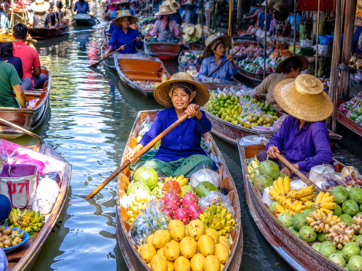 Wooden boats laden with tropical fruit and grilled food navigating narrow canals at a Bangkok floating market at sunrise