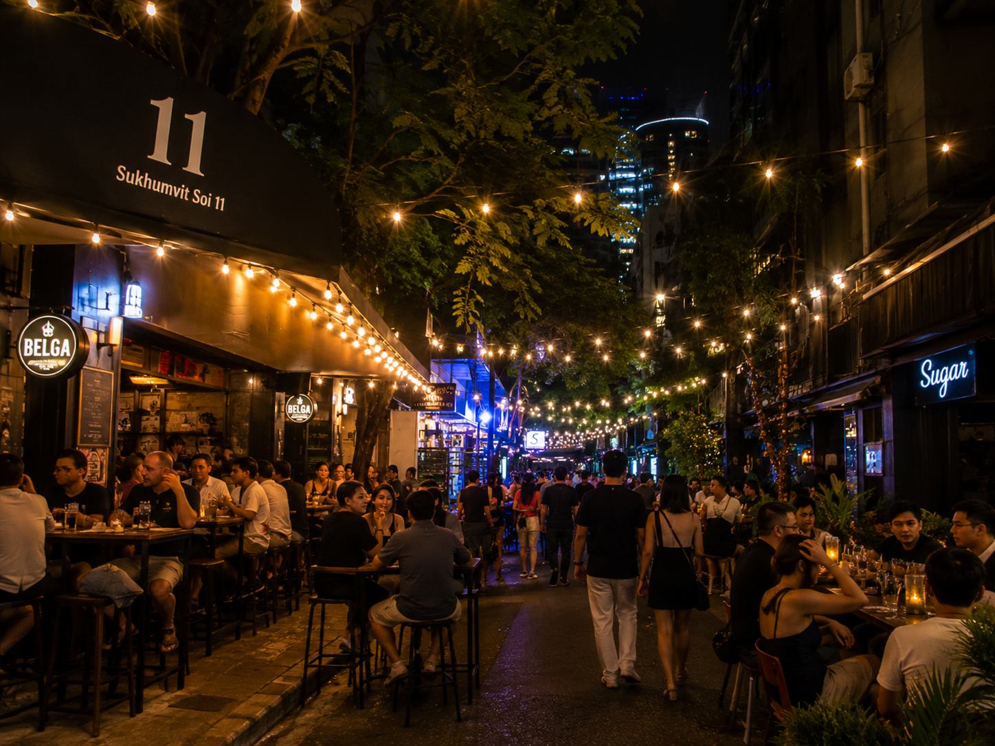 Sukhumvit Soi 11 at night with illuminated bar signs and restaurant terraces lining both sides of the street in Bangkok